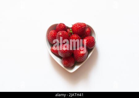 Delicious red strawberries in heart shaped bowl with top view. Healthy sweet berries isolated on white background, selective focus. Stock Photo