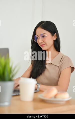 Portrait of a beautiful asian woman with eyeglasses sits in her office workspace, typing on keyboard, working on her business assignment. Stock Photo