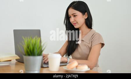 Attractive Asian young female freelancer or female office worker sits in her workplace and using laptop computer. Stock Photo
