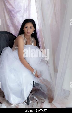 A beautiful Asian woman wearing a gold sequin top and tulle skirt and posing amongst draped fabric Stock Photo