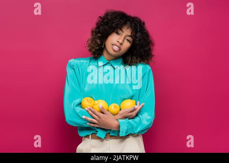african american woman in turquoise blouse holding fresh lemons isolated on pink Stock Photo