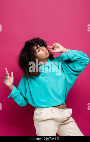 trendy african american woman in turquoise blouse pointing with fingers isolated on pink Stock Photo