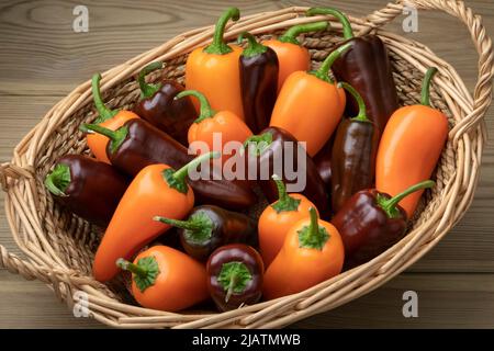 Basket with whole fresh orange and chocolate mini pointed bell peppers close up on wooden background Stock Photo