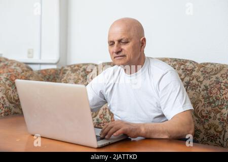 Cheerful satisfied retired mature person sitting at table in the kitchen working on computer received good positive news from bank using laptop for Stock Photo