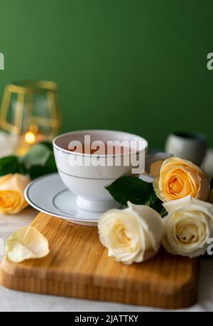 A cup of herbal tea and a bouquet of roses on a green background, Vertical Stock Photo