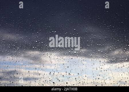Raindrops on the window glass on blurred background of sky with storm clouds. Beautiful water drops, rainy weather Stock Photo