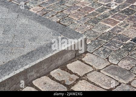 corner of a pedestrian sidewalk made of granite curb and stone rectangular brick tiles nearby a road paved with rough cut paving slabs close-up, nobod Stock Photo