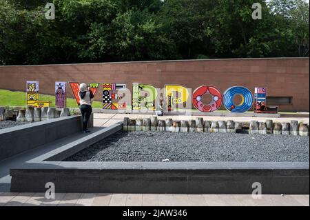 Liverpool, England, Uk. A woman wwearing a headscarf takes a photo on her phone of a friend next to the letters spelling Liverpool. Stock Photo