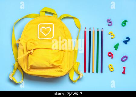 Back to school, education concept. Yellow backpack, pencils, numbers isolated on blue background. Top view. Copy space Flat lay composition. Stock Photo