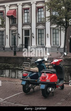 Leiden, Netherlands - July 25, 2021: White and blue scooter is parked in Leiden along the Old Rhine with a canal, with a beautiful house in the backgr Stock Photo