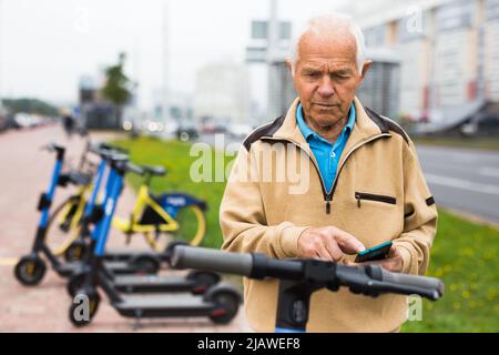 Old man using smartphone to activate e-scooter Stock Photo