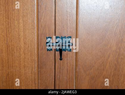 Black metal deadbolt on brown wooden door, closed without a key Stock Photo