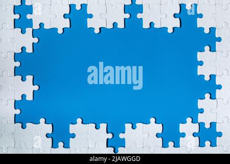 Framing in the form of a rectangle, made of a white jigsaw puzzle. Frame text and jigsaw puzzles. Frame made of jigsaw puzzle pieces on blue backgroun Stock Photo