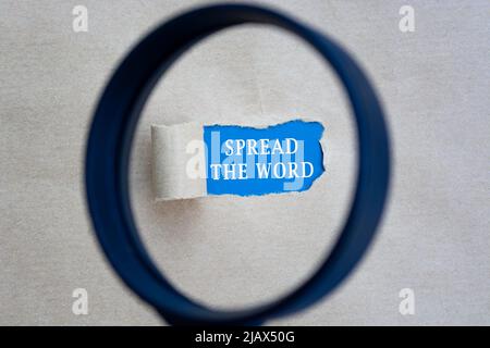 Spread the word text on torn hole in the sheet of brown paper on blue background with magnifying glass. Website, search and network concept. Stock Photo