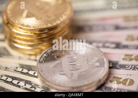 Piled up gold bitcoin coins next to silver bitcoin on top of US dollar bills. 50 dollar banknotes, paper money from America Stock Photo