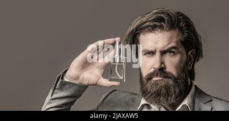 Masculine perfume, bearded man in a suit. Male holding up bottle of