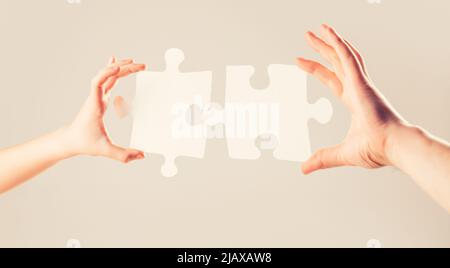 Mens and childs hands connecting puzzles. Hands connecting puzzle. Puzzles. Hand of the child and hand of mother fold puzzle, closeup. Hands hold Stock Photo
