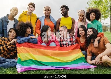 Happy diverse friends holding LGBT rainbow flag having fun together outdoors - Main focus on bald girl face - Diversity community concept Stock Photo