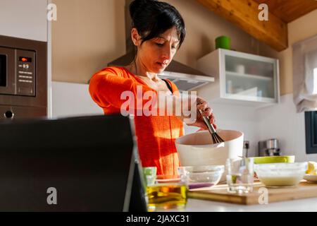 Woman in orange sweater whisking eggs on a white bowl. Stock Photo