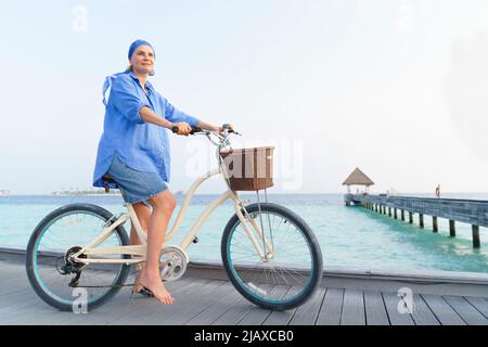 A woman on a bicycle on the ocean in the Maldives. Stock Photo