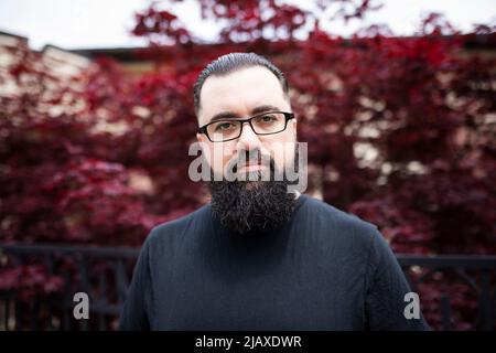 Headshot of a bearded man with glasses in front of a red maple tree Stock Photo