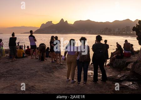 Beautiful view to people enjoying the sunset from the rocks in Ipanema Stock Photo