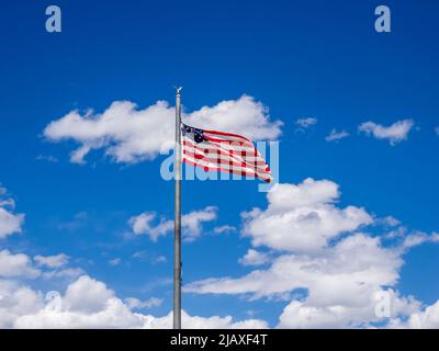 America flag flying on a flagpole aganist a blue sky with white puffy clouds Stock Photo