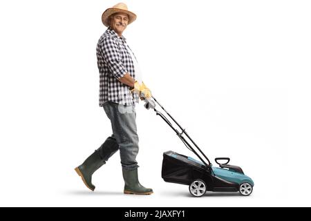 Full length profile shot of a mature man with a straw hat and boots using a lawn mower isolated on white background Stock Photo