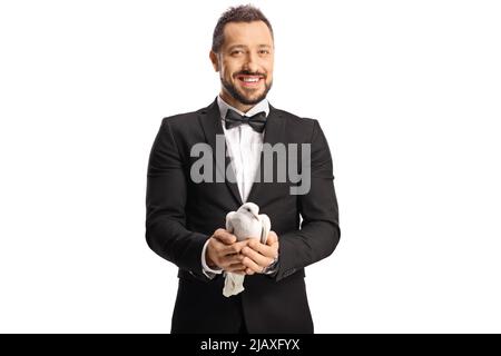 Smiling elegant young man in suit and bow-tie holding a white dove in his hands isolated on white background Stock Photo