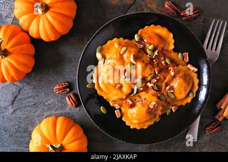 Pumpkin filled ravioli pasta with nuts and pumpkin seeds. Table scene, above view on a dark background. Stock Photo