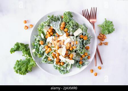 Vegetarian Caesar salad with chickpeas, kale and a yogurt dressing. Top view over a white marble background. Plant based food concept. Stock Photo