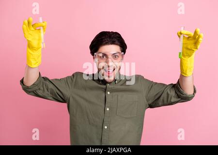 Photo of funny guy hold two chemical tube raise hands wear goggles gloves khaki shirt isolated pink color background Stock Photo