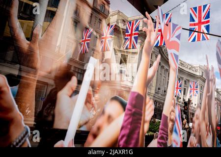 Images of celebration arms in the air form a window display, part of the Queen's Platinum Jubilee celebrations in retailer 'Hackett's' window, merging with a background of shoppers and hanging Union Jack flags above Regent Street, on 1st June 2022 in London, England. Queen Elizabeth II has been on the UK throne for 70 years, the longest-serving monarch in English history and Union Jack flags can be seen everywhere around the country in the week before the Jubilee weekend.