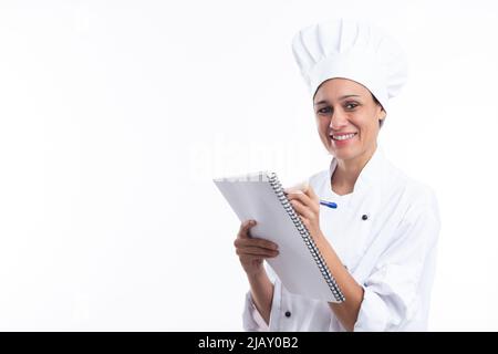 Happy latina cook writing down recipes in her notebook looking at camera isolated on white background with copy space. Stock Photo