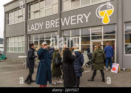 The "Lady Brewery" lettering with the brewery's yellow-and-white logo adorns the grey facade of the building in the Grandi harbour district of Reykjavik, Iceland; several guests stand and talk in front of the entrance. Design March in Reykjavik is the country's largest design festival, for which Lady Brewery has brewed the festival beer for several years. Stock Photo