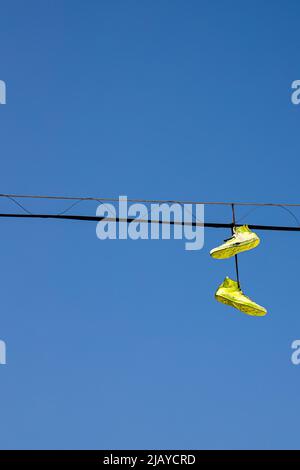 Hanging yellow shoes on electricity wires, sneakers on the power line with blue sky on the background Stock Photo