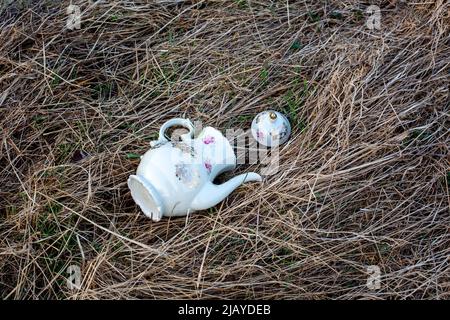 old antique porcelain tea pot lying on the floor outside in hay Stock Photo