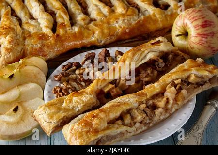 Pieces of delicious homemade pie with apples and nuts on a white plate against a background of strudel, apples and nuts. Pie and ingredients Stock Photo