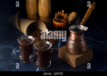 Turk and two cups of hot coffee with spices and coffee beans on a dark background Stock Photo