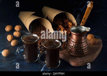 Turk and two cups of hot coffee with spices, nuts and coffee beans on a dark background Stock Photo