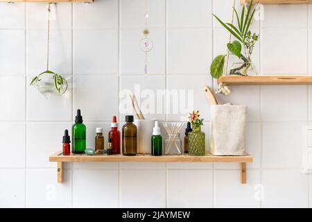 Wooden shelves with cosmetics and toiletries against white tiled wall. Hanging glass pots with green plants. Trendy biophilic and eco friendly minimalistic design Stock Photo