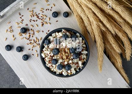 Whole grain oatmeal porridge with flax seeds, blueberries, cottage cheese and ears of wheat on a white painted wooden tray. Vegetarian eating Stock Photo