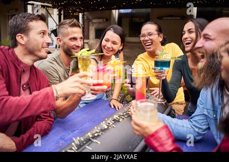 Young people cheers and having fun. Group of happy friends drinking and toasting cocktails at brewery bar terrace pub. Stock Photo