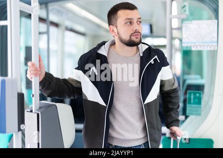 Young bearded man with suitcase riding in streetcar Stock Photo