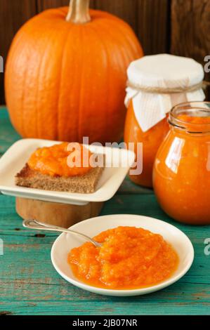 Homemade yummy pumpkin jam in white plate, in glass jars with whole pumpkin on wooden table vertical Stock Photo