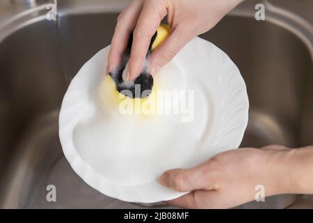 Woman washes a plate in the kitchen under the sink. Top view close up. Stock Photo