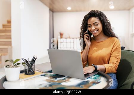 Smiling black woman working and talking on phone at home Stock Photo