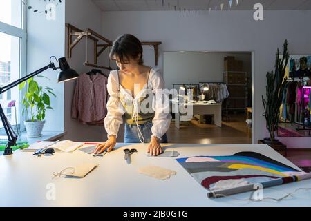 Young designer woman dressmaker work on new clothes collection in studio workshop. Small business. Stock Photo