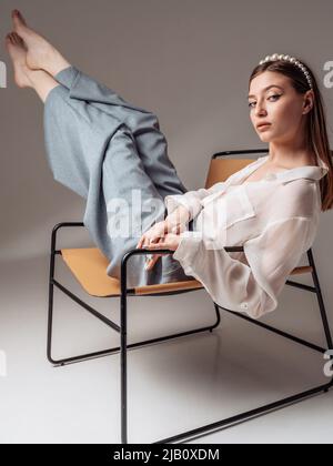Feet up. Casual young woman sits barefoot on a comfortable armchair, relaxes, raises her legs. vertical. Stock Photo