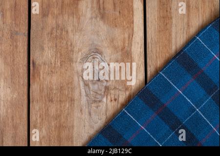 The blue checkered fabric lies against the wooden background. A towel or kitchen napkin on the rough boards or kitchen table. Stock Photo
